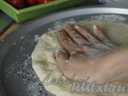 Подошедшее тесто делим на 2 части. Одну часть теста кладём в центр формы для выпечки и, придавливая руками, начинаем растягивать к краям формы. Для правильного приготовления пиццы тесто надо не раскатывать, а растягивать руками.
