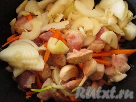 К обжаренному мясу добавьте морковь, лук и целые зубчики чеснока (прямо со шкуркой). Перемешайте и потушите ещё немного.
