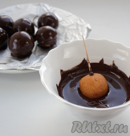 Окунуть каждый шарик в растопленный шоколад, выложить на застеленную фольгой тарелку и убрать в холодильник до застывания шоколада.