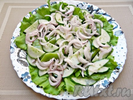 На плоскую тарелку выложить листья салата, огурцы и лук.
