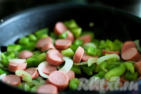Нарежьте лук полукольцами, перец квадратиками, а сосиски кружочками. Налейте немного оливкового масла на сковороду и обжарьте недолго на ней овощи с сосисками. Добавьте специи для аромата.