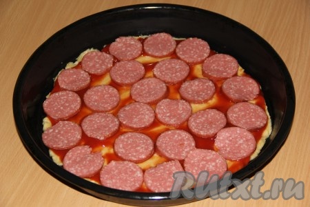 Основу для пиццы из бездрожжевого теста смазать томатным соусом, выложить тонкие кружочки колбасы.
