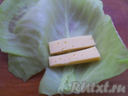 Утолщенную часть капустных листьев отбить молоточком. Поместить по 2 кусочка твердого сыра, порезанного брусочками.
