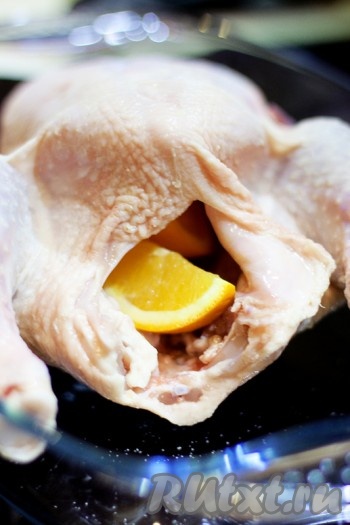 Вложите дольки апельсина, дольки чеснока, разрезанные пополам, и бутоны гвоздики в курицу.
