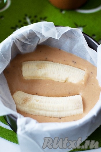 Подготовьте формы или одну форму, застелите пекарской бумагой и вылейте в нее половину теста. Разрежьте банан вдоль и пополам (на 4 части). Уложите их в форму на тесто.
