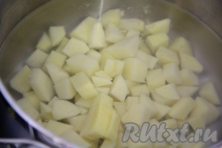 В кастрюлю влить воду и поставить на огонь. Картофель почистить и нарезать мелкими кубиками, отправить в воду и довести до кипения.
