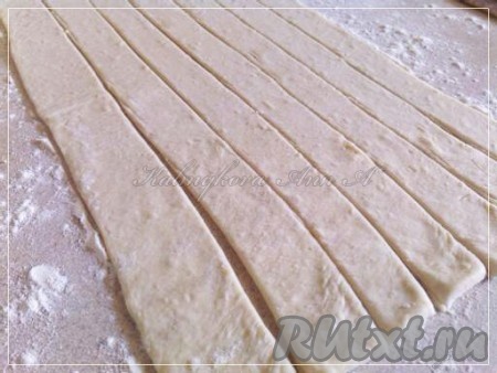 Разморозить слоеное дрожжевое тесто. Присыпать рабочую поверхность мукой, слегка раскатать пласт теста и нарезать полоски шириной около 2 см.
