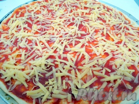 Сыр натираем на крупной тёрке. Пиццу, смазанную томатной пастой, посыпаем половиной сыра. Вторую половину сыра отставляем.