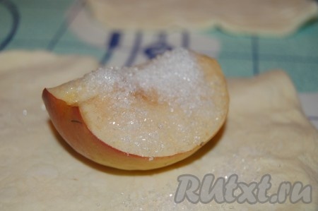 Положить дольку яблока на кусок раскатанного теста, сверху посыпать сахаром.