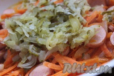 Соленый огурец натереть на крупной терке и добавить в сковороду к сосискам, луку и моркови.
