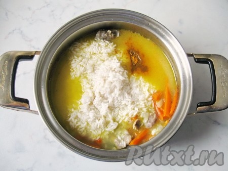 Рис хорошо промыть в проточной воде. Выложить в миску и залить на час горячей водой, немного посолить. После всыпать рис в кастрюлю к желудкам и овощам. Посолить и поперчить по вкусу, добавить сухую куркуму. Разровнять ложкой рис.
