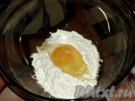 Для приготовления затирки 140 грамм муки выложить горкой в глубокую миску, в центр всыпать щепотку соли и соду, разбить сырое яйцо.