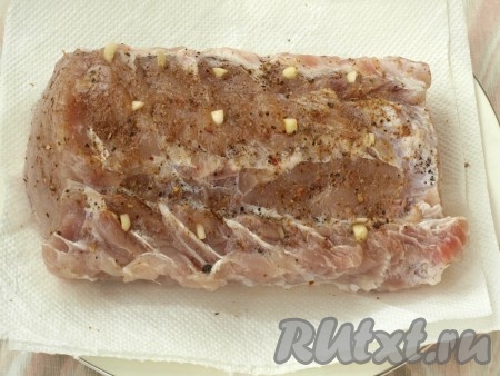 По истечении времени мясо обсушить салфетками, сделать проколы ножом, нашпиговать чесноком, натереть перцем и приправой для мяса.
