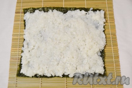 Выложить на коврик для суши лист нори так, чтобы гладкая сторону была внизу. Выложить тонким слоем рис. 
